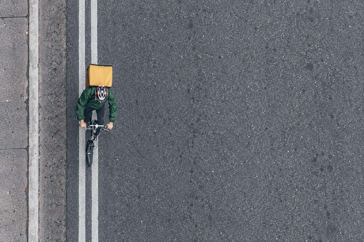 Top-down view of a cyclist with a delivery backpack riding along an almost empty asphalt street.