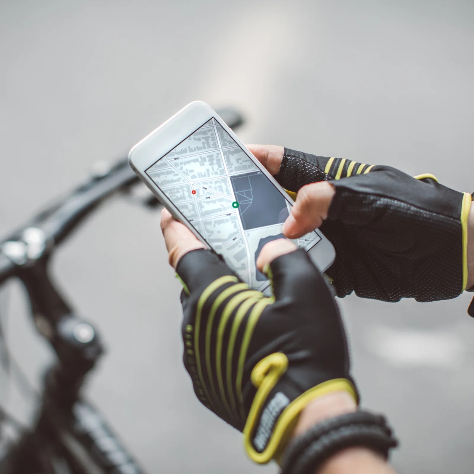 Close-up of two gloved hands holding a phone over bicycle handlebars, with a street map and a route on the screen.